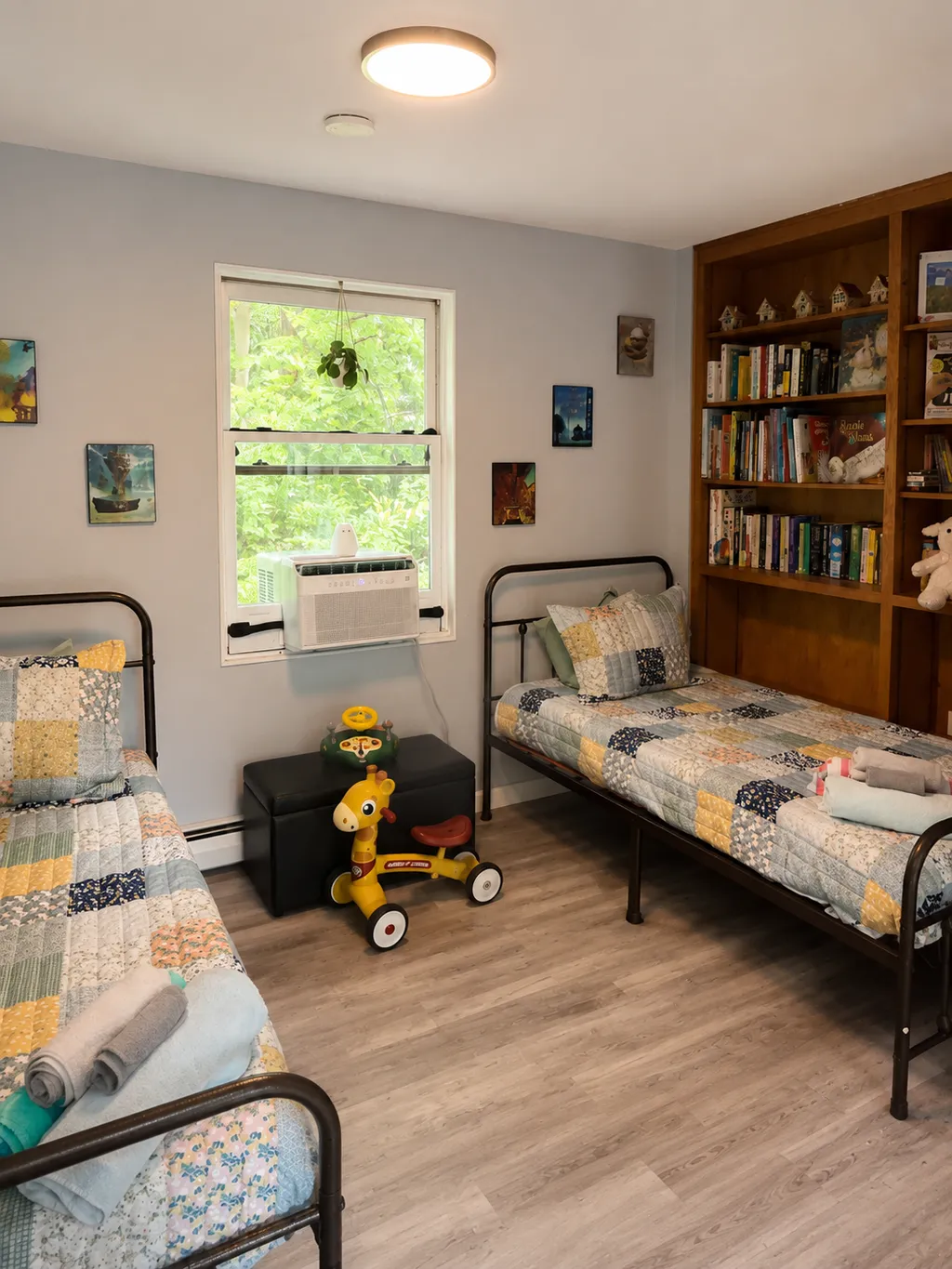 Two twin beds in a room with a bookshelf, a window, and a toy.