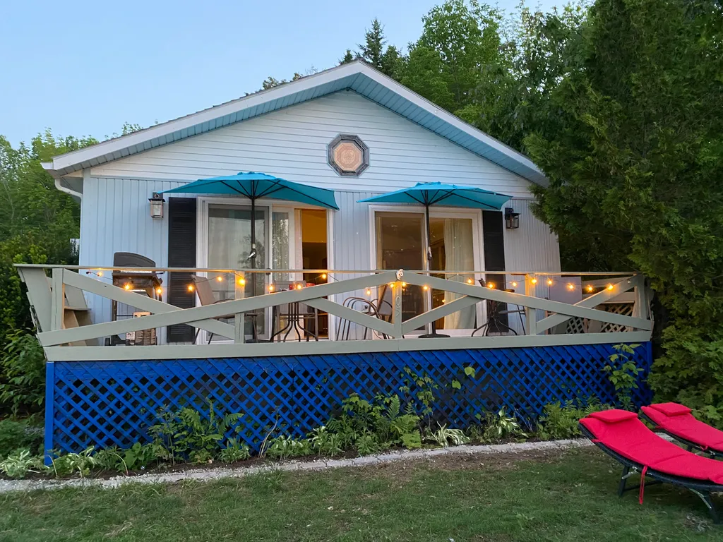 A small white house with a blue fence and two blue umbrellas on the porch.