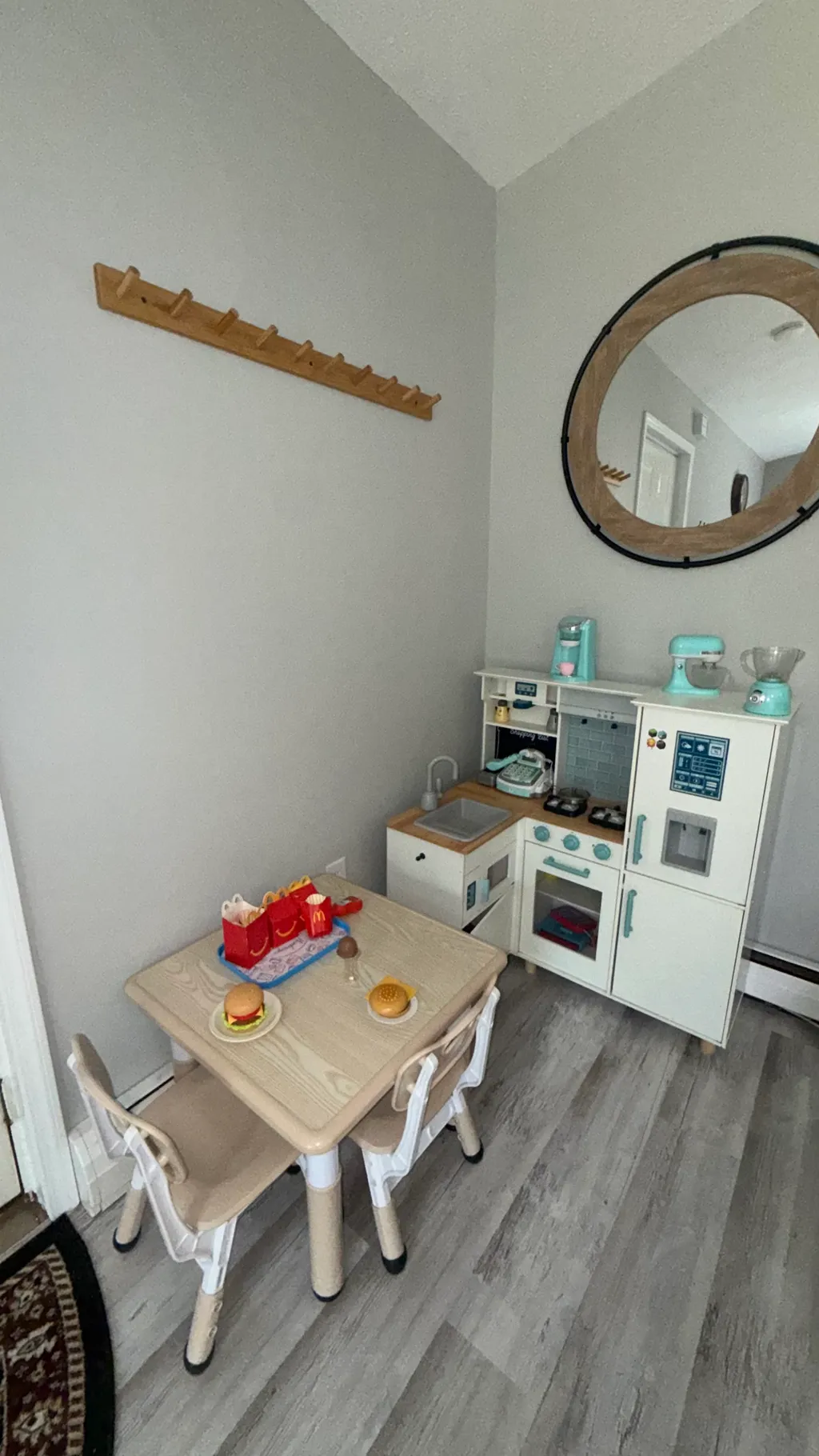 A small kitchen area with a toy stove, sink, and a round mirror above.