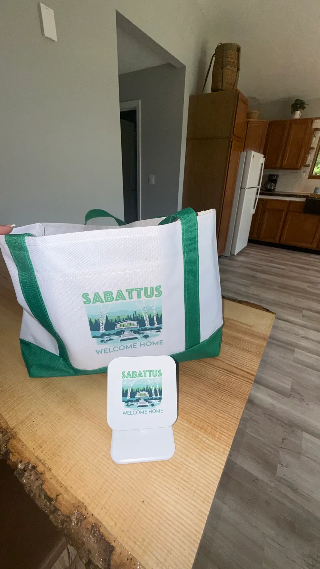 A green and white tote bag with "Sabbatus" text sits on a wooden table.